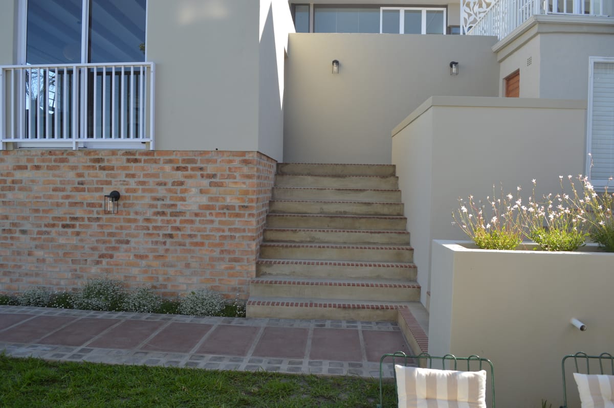 Brick steps rising to the private entrance, with planting and garden chairs in the foreground