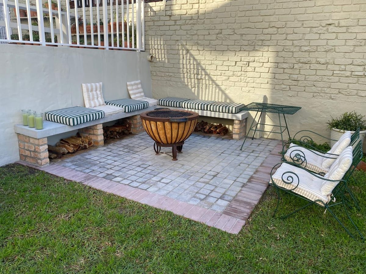 Walled garden with a copper fire bowl on brick paving and cushioned benches