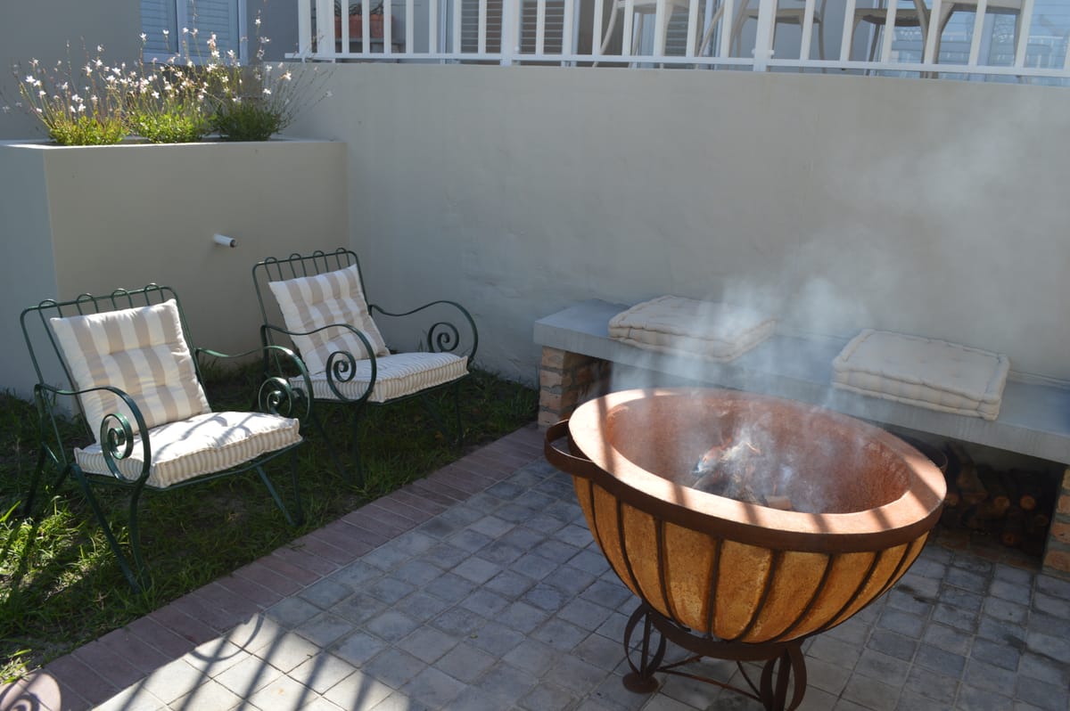 A copper fire bowl alight in the walled garden, with green metal chairs and a built-in bench