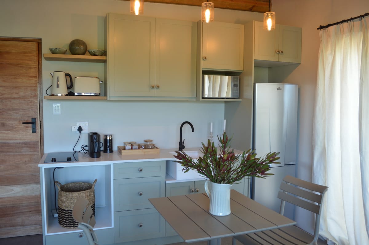 The kitchen with sage green cabinetry, glass pendant lights and a dining table set with proteas