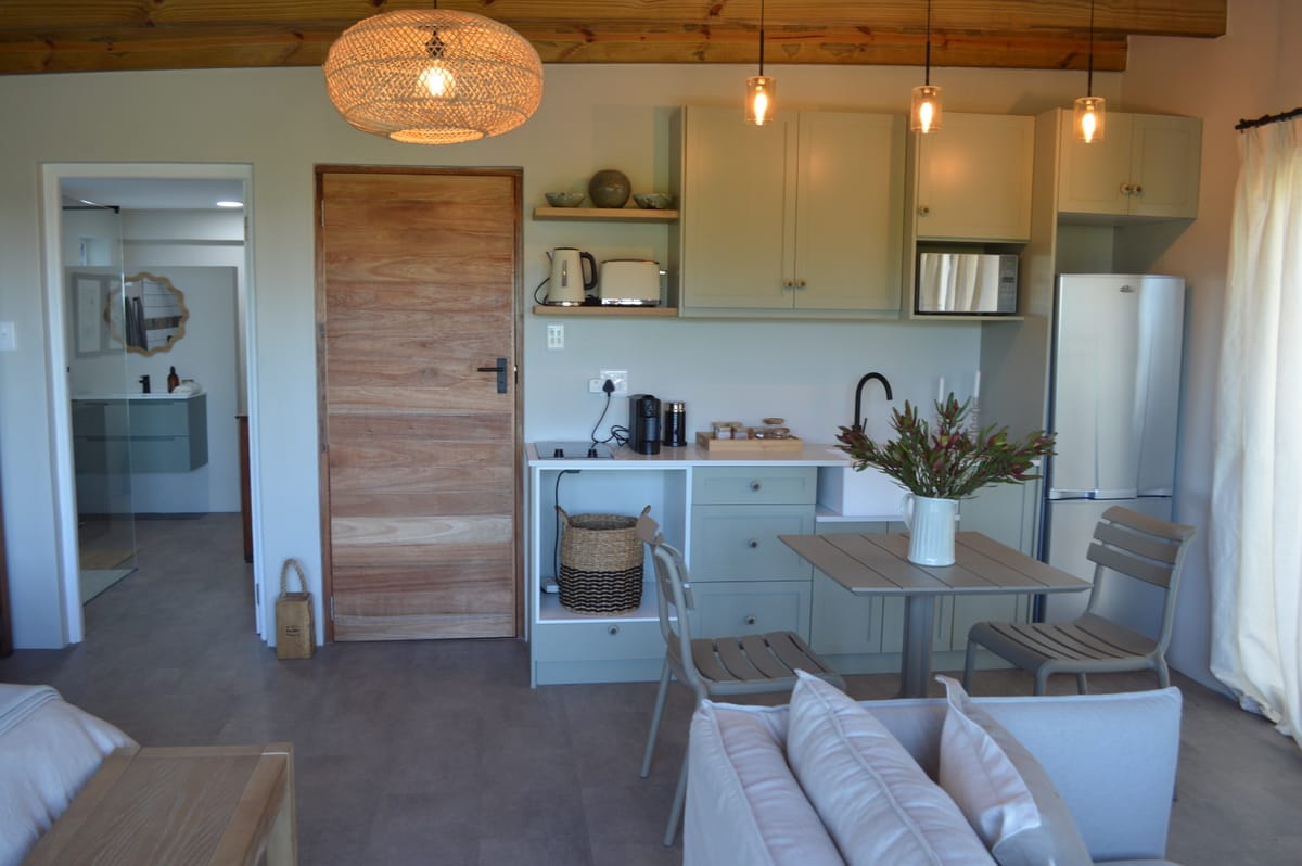 The kitchenette with sage cabinetry, dining table and a vase of proteas