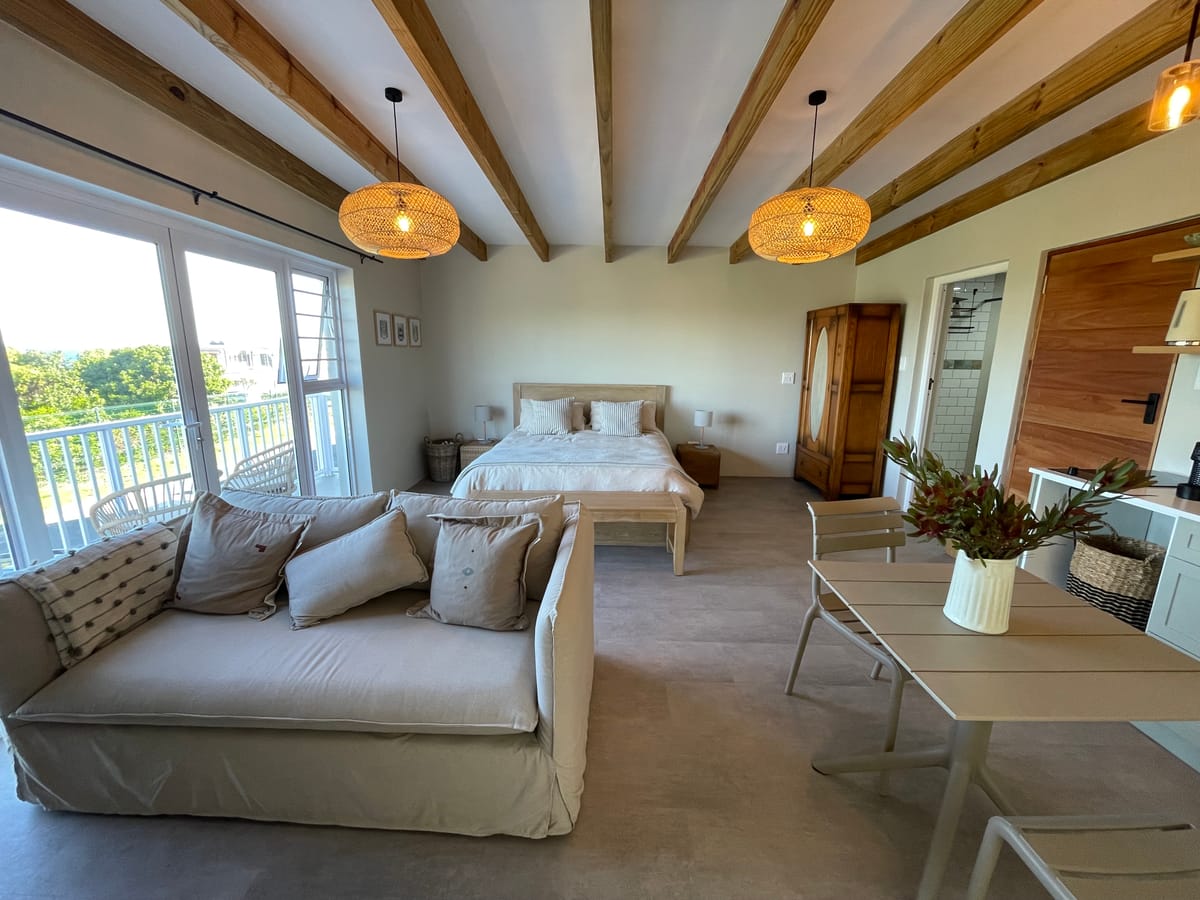 Open-plan living area with exposed pine beams, rattan pendants and French doors to the balcony